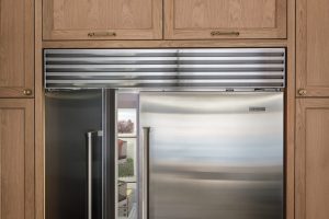 A stainless steel refrigerator with one door slightly open, built into wooden cabinetry, revealing some food items inside—perfect for homes seeking luxury kitchen appliance service.