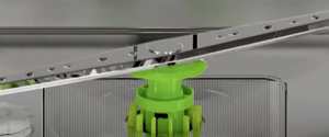 Close-up view of a green plastic rotating arm mechanism inside a dishwasher, shown during a luxury kitchen appliance service, highlighting part of the sprayer and filter assembly.