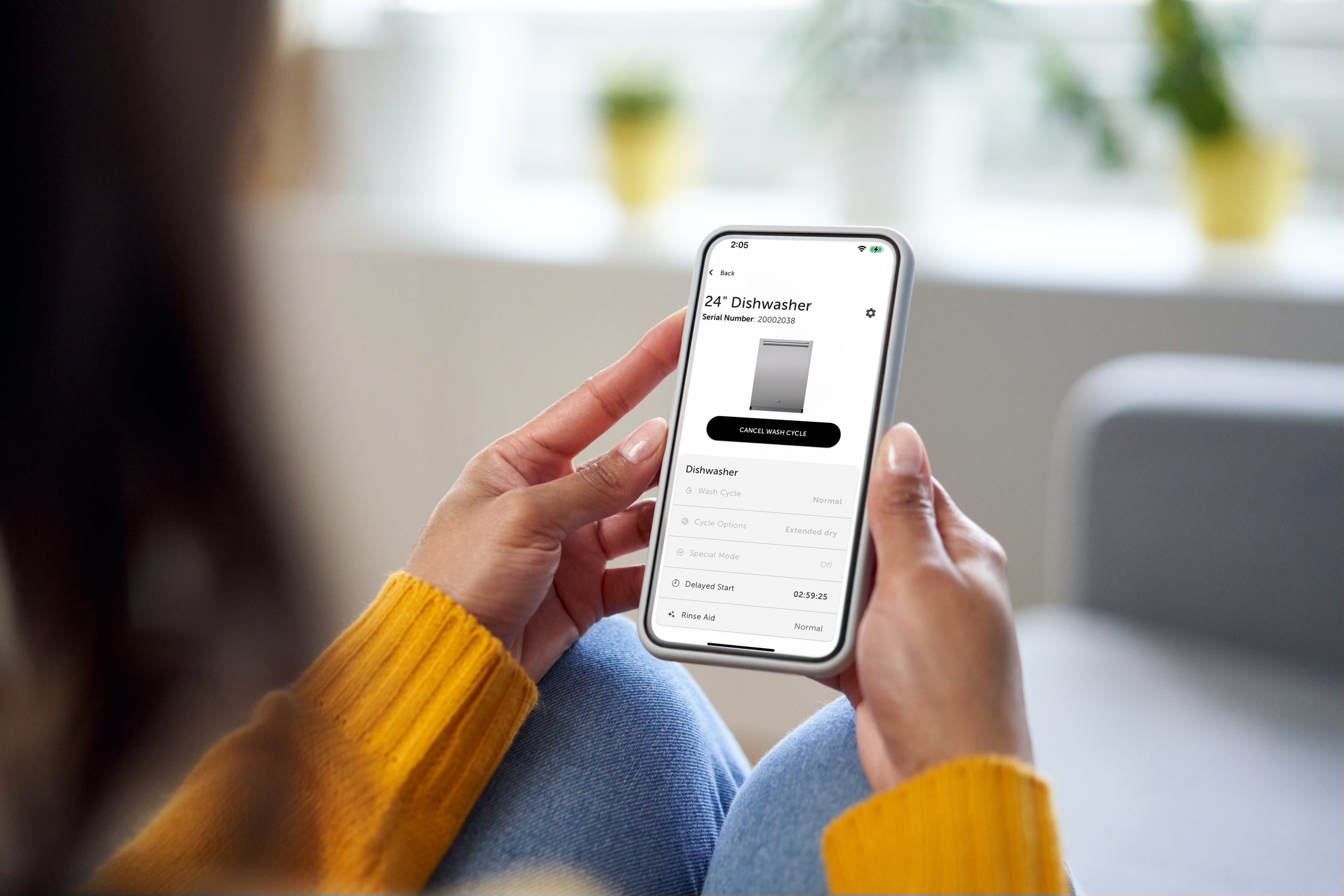 Person holding a smartphone with an app open, displaying details for a 24" dishwasher, including product image, description, and purchase options.