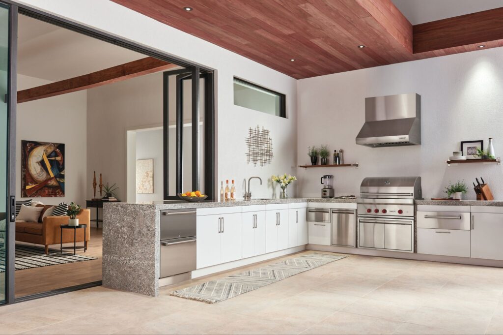 Modern kitchen with stainless steel appliances, white cabinets, and granite countertops, plus a Cove dishwasher—learn how to clean the filter on a Cove dishwasher for peak performance—all seamlessly connected to the living area by large glass doors.