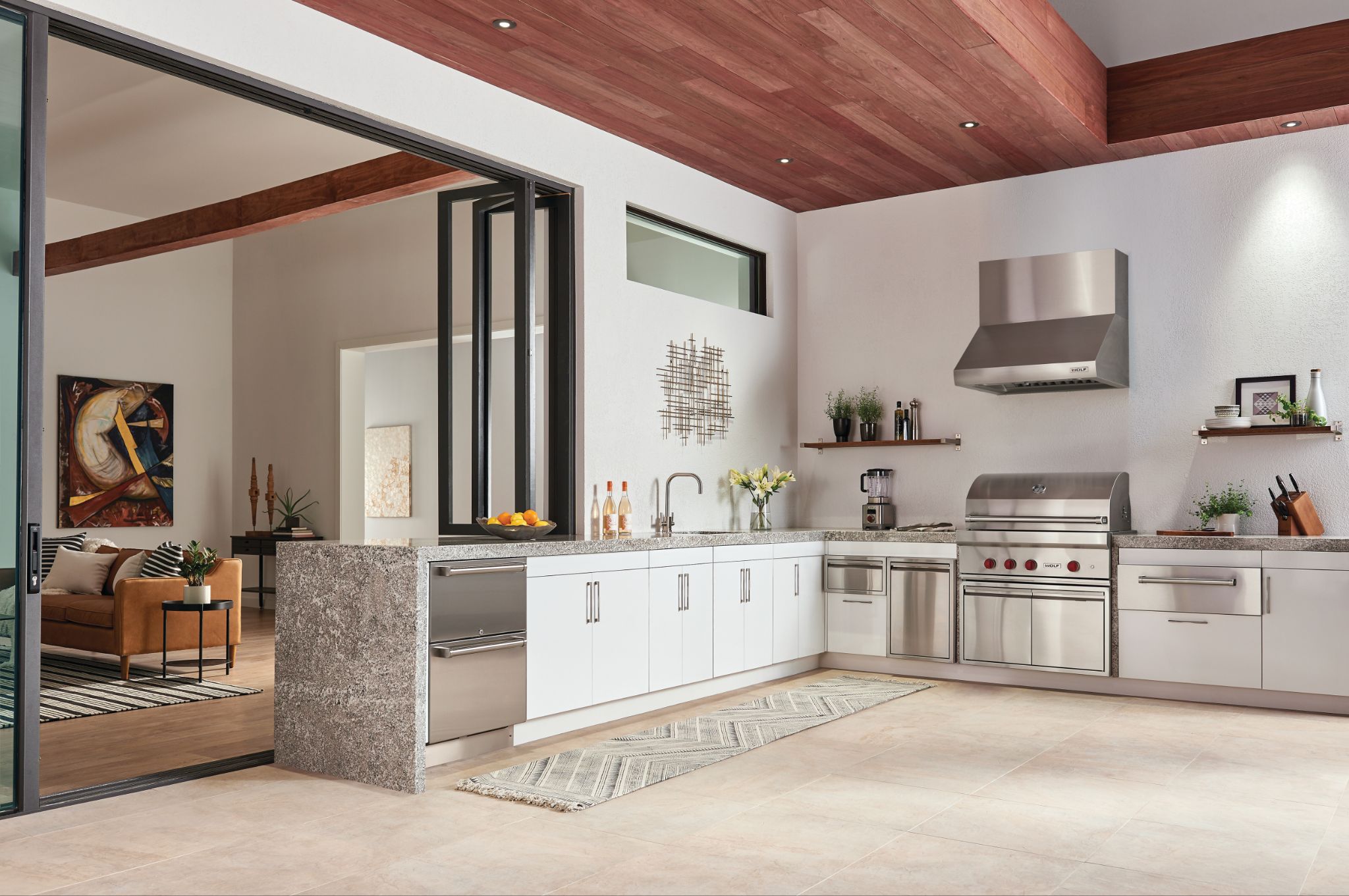 Modern kitchen with stainless steel appliances, white cabinets, and granite countertops, plus a Cove dishwasher—learn how to clean the filter on a Cove dishwasher for peak performance—all seamlessly connected to the living area by large glass doors.